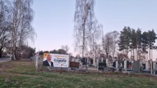 Plakat wyborczy na ogrodzeniu cmentarza